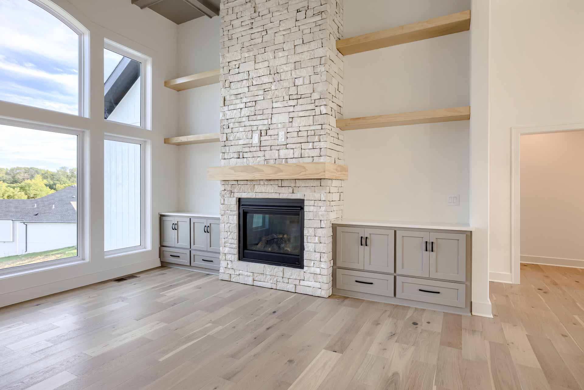 Stone fireplace in high-ceiling living room with custom built-ins.